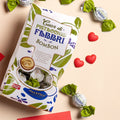 Immagine di San Valentino che raffigura la confezione di Bom Bon Pistacchio su un ripiano, con praline e cuoricini sparsi.