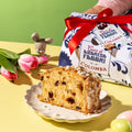 Immagine verticale con fetta di colomba Cuor di Amarena Fabbri impiattata e relativo packaging a fianco. Elementi pasquali sullo sfondo come fiori e ovette.