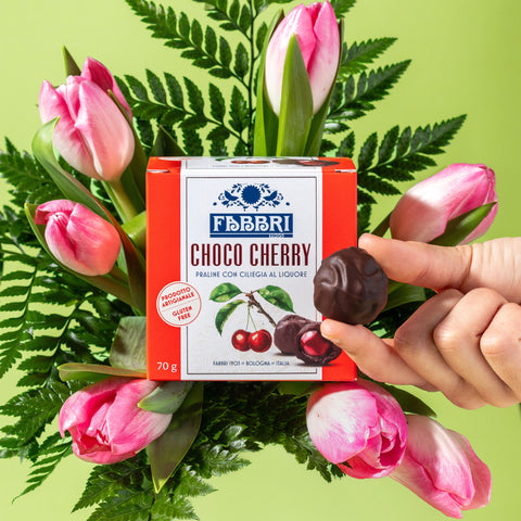 Mazzo di tulipani con confezione praline Choco Cherry al centro e mano che tiene tra le dita una pralina sconfezionata